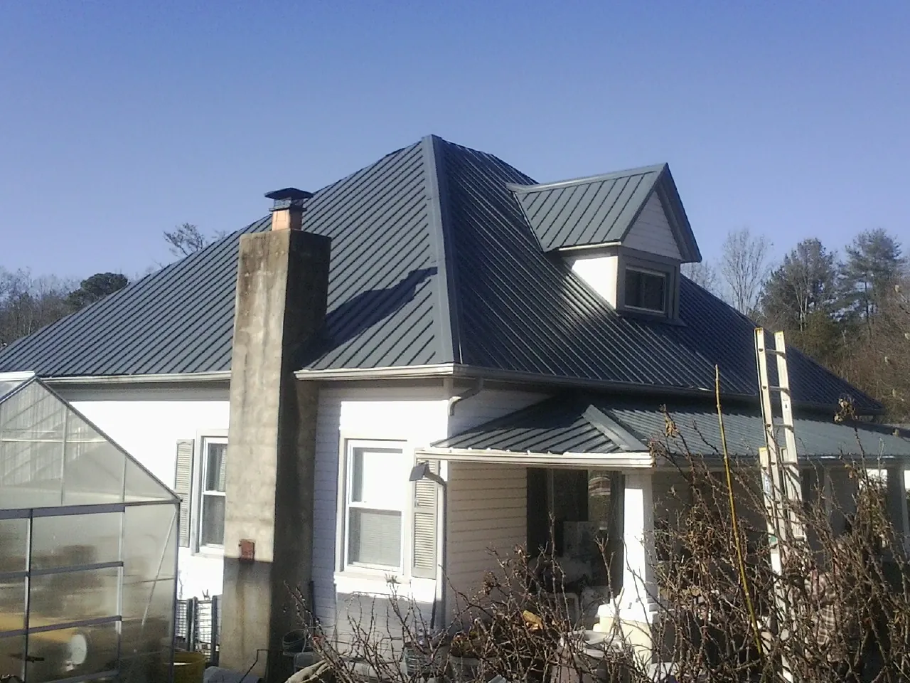 Dark blue standing seam metal roof on a white farmhouse with dormer — Slate & Tile Roof Repair by Roofing Brothers in Bellefonte