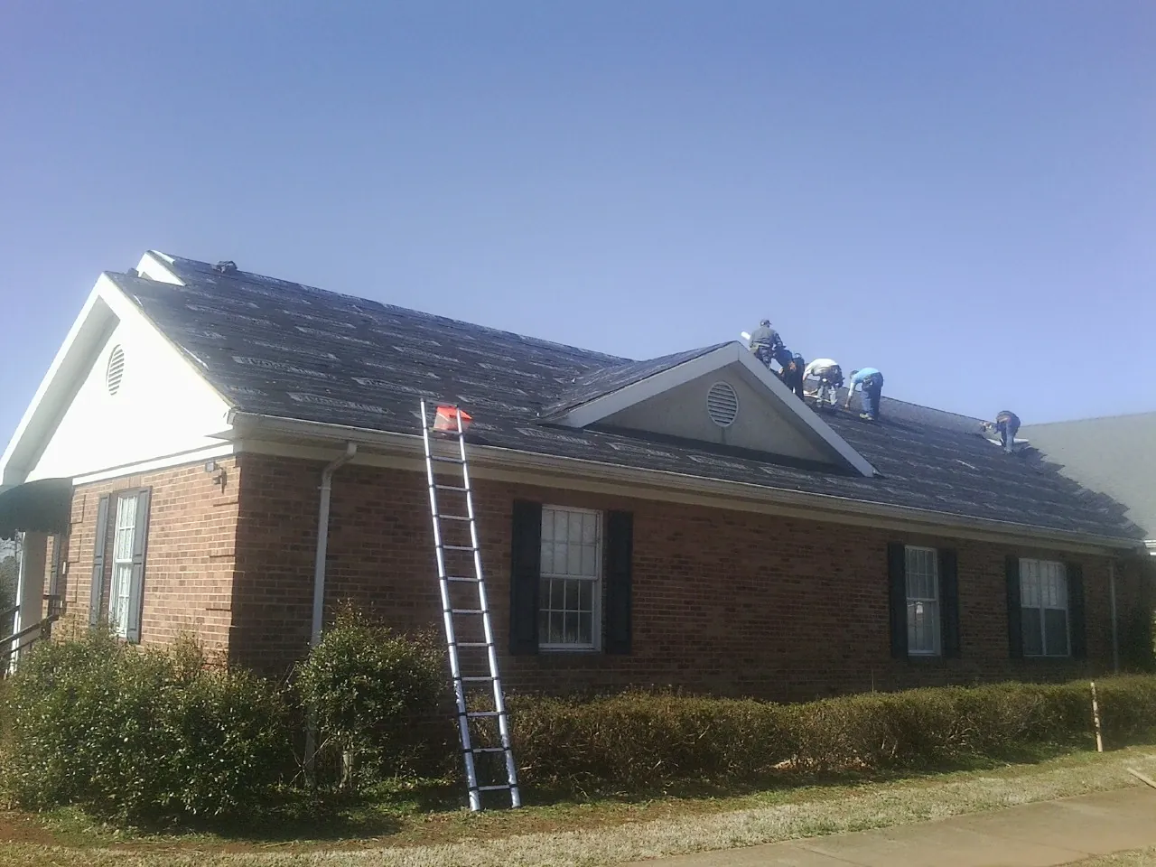 Crew tearing shingles off a brick ranch roof with a ladder set — Metal Roof Repair work by our crew in Bellefonte