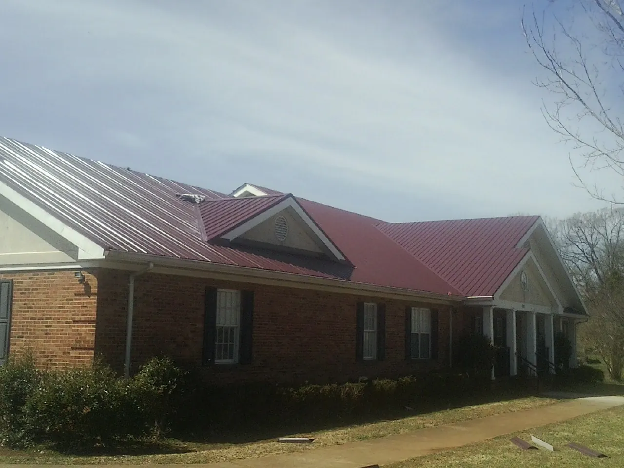 Red metal roof with gabled entries on a long brick building, from a Hail Damage Roof Repair job in Bellefonte