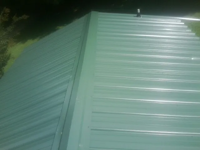New green metal panels meeting at the ridge of a roof — Flat Roof Repair work by our crew in Bellefonte