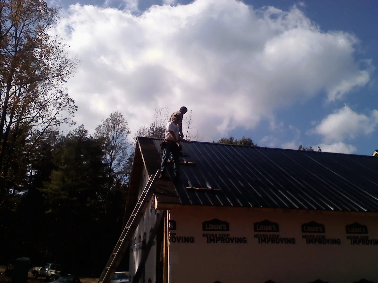 Roofer fastening dark metal panels high against a cloudy sky, from a Roof Inspection job in Bellefonte