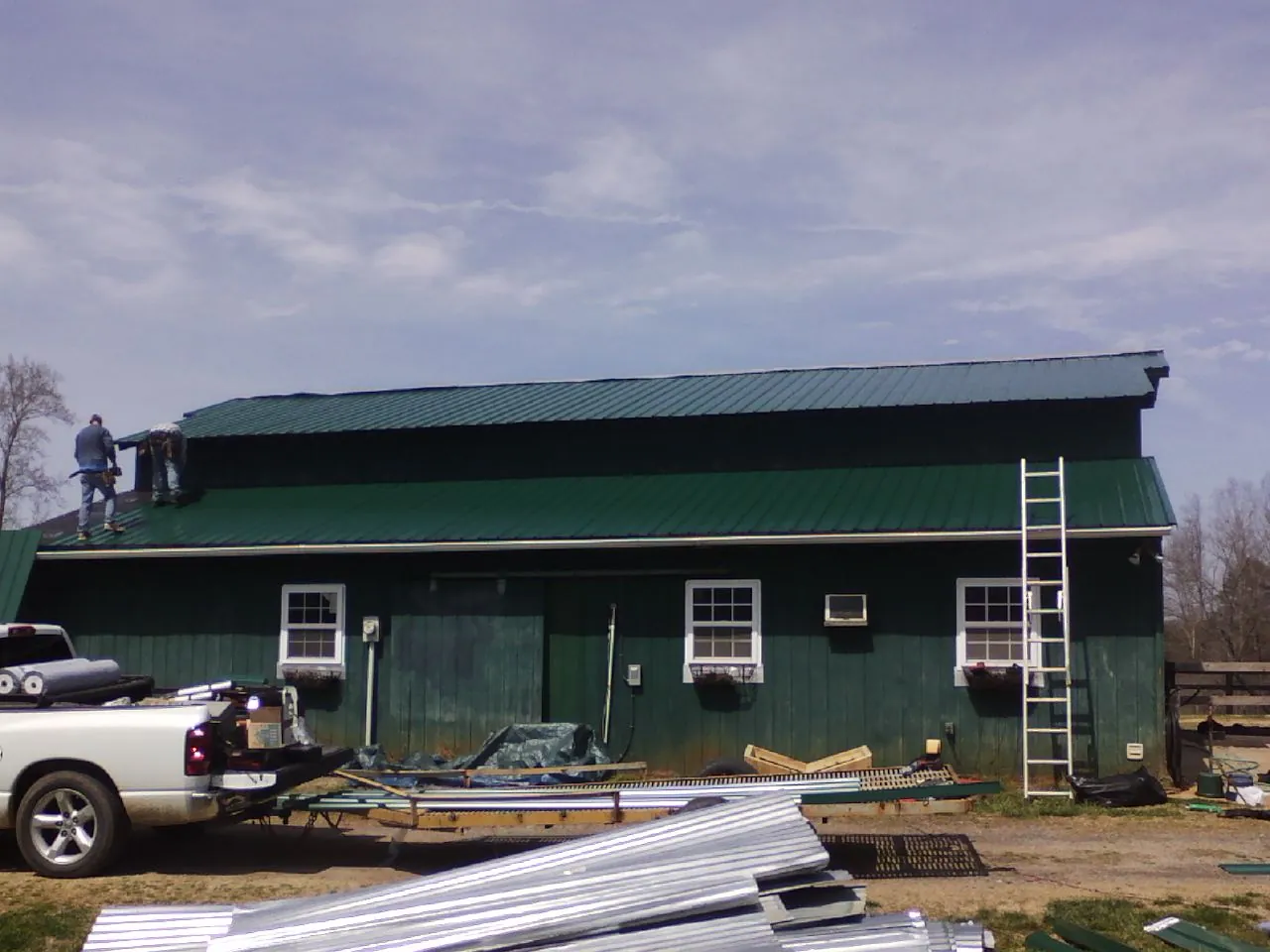 Crew installing green metal roofing on a large green barn in Bellefonte