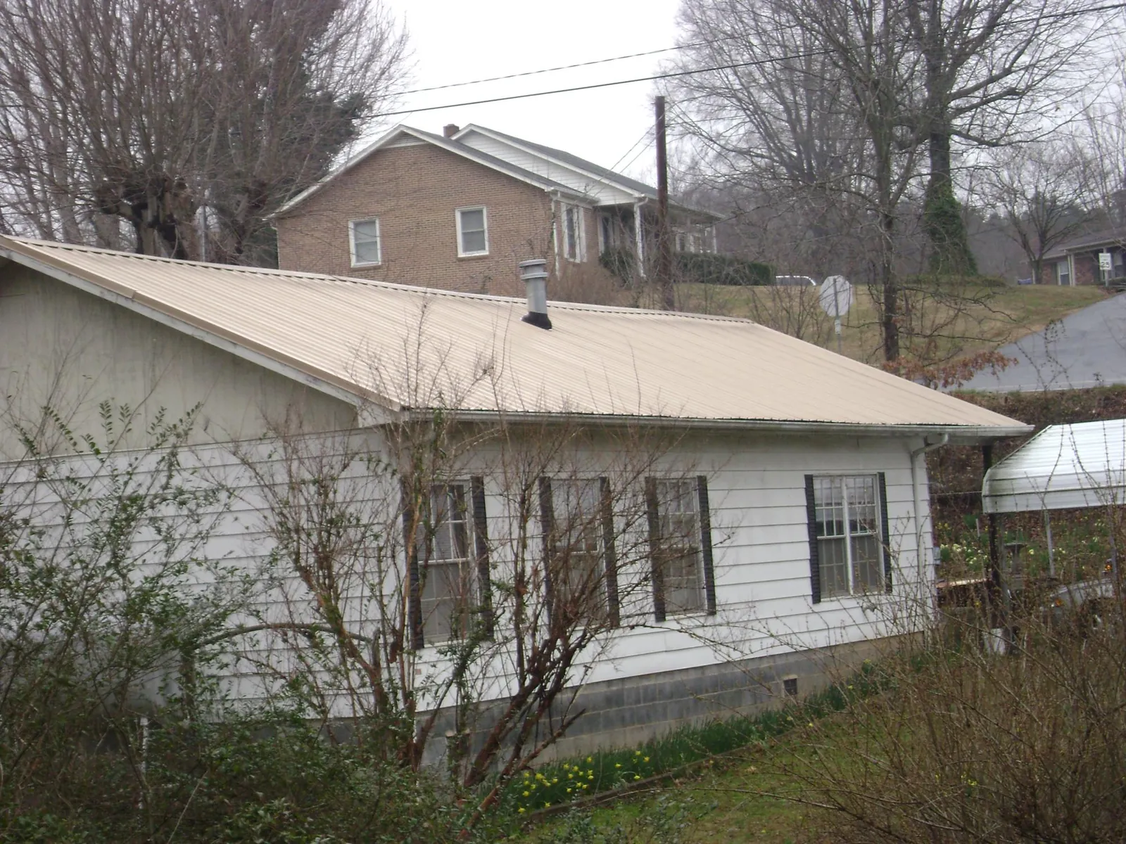 Tan metal roof on a white sided house set into a hillside — Commercial Roofing by Roofing Brothers in Bellefonte
