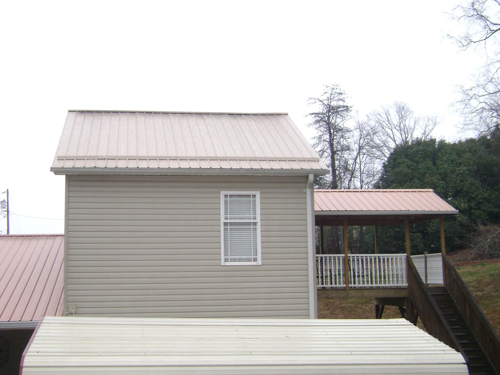 Tan metal roofs on a two story addition and attached porch, from a Roof Replacement job in Bellefonte